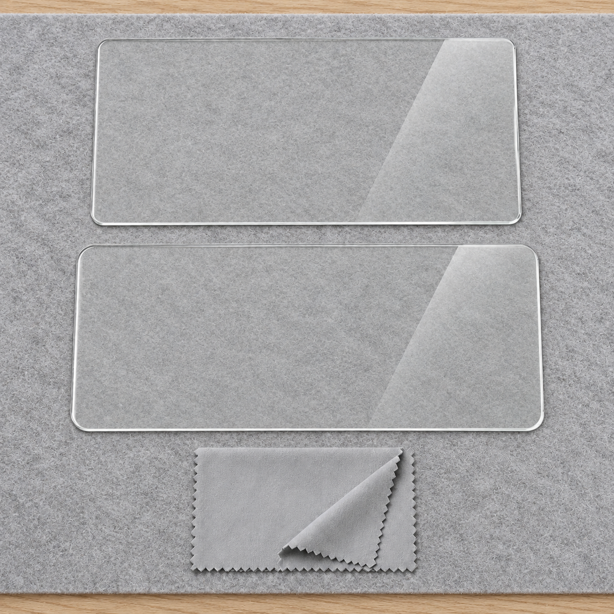 Two uninstalled clear display protector sheets and a folded gray cloth on a plain felt inspection mat.