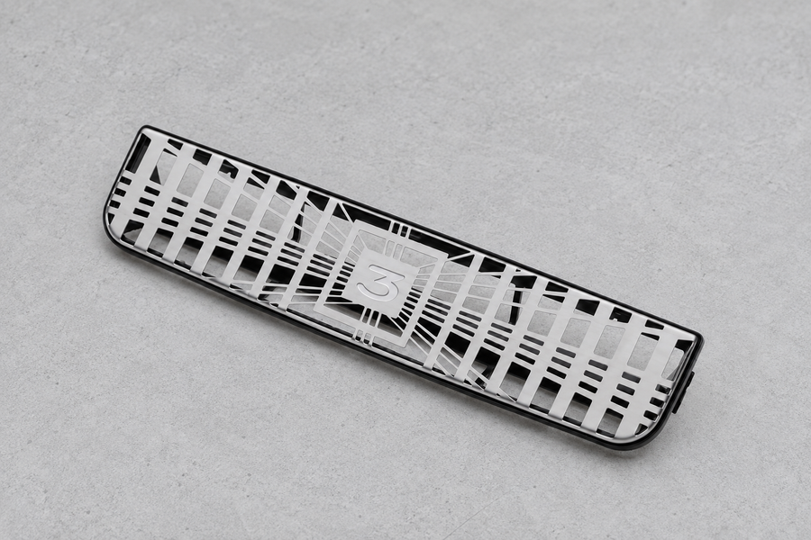 Silver openwork vent grille resting on a grey inspection surface