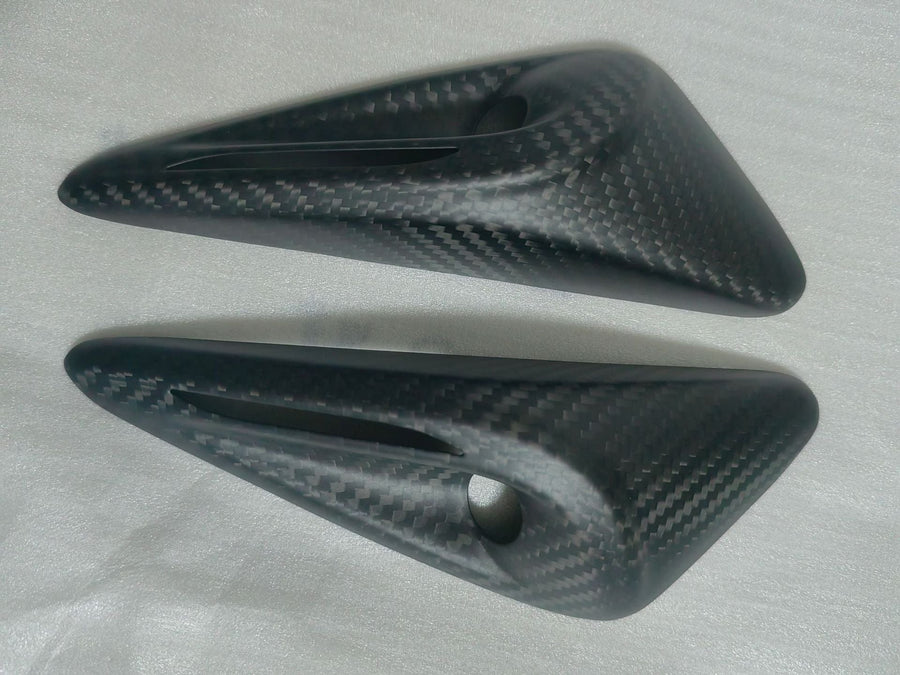 Two carbon-style camera-housing trim pieces with open apertures on a foam sheet