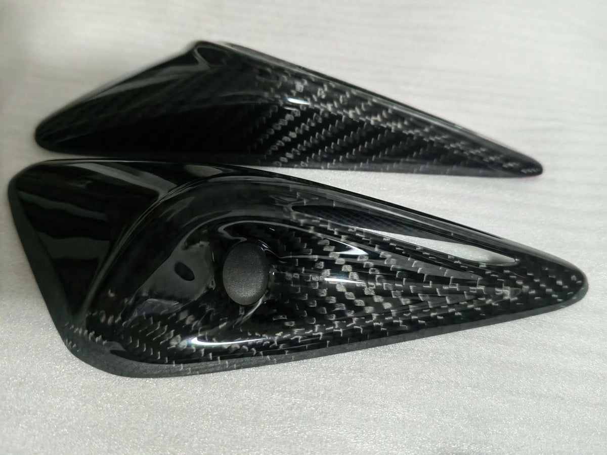Pair of glossy exterior camera trim covers with circular lens openings on protective foam