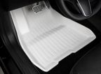 A white molded floor mat in a driver footwell, with the pedals and lower steering-wheel rim visible.