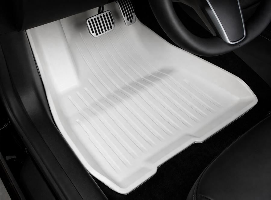 A white molded floor mat in a driver footwell, with the pedals and lower steering-wheel rim visible.