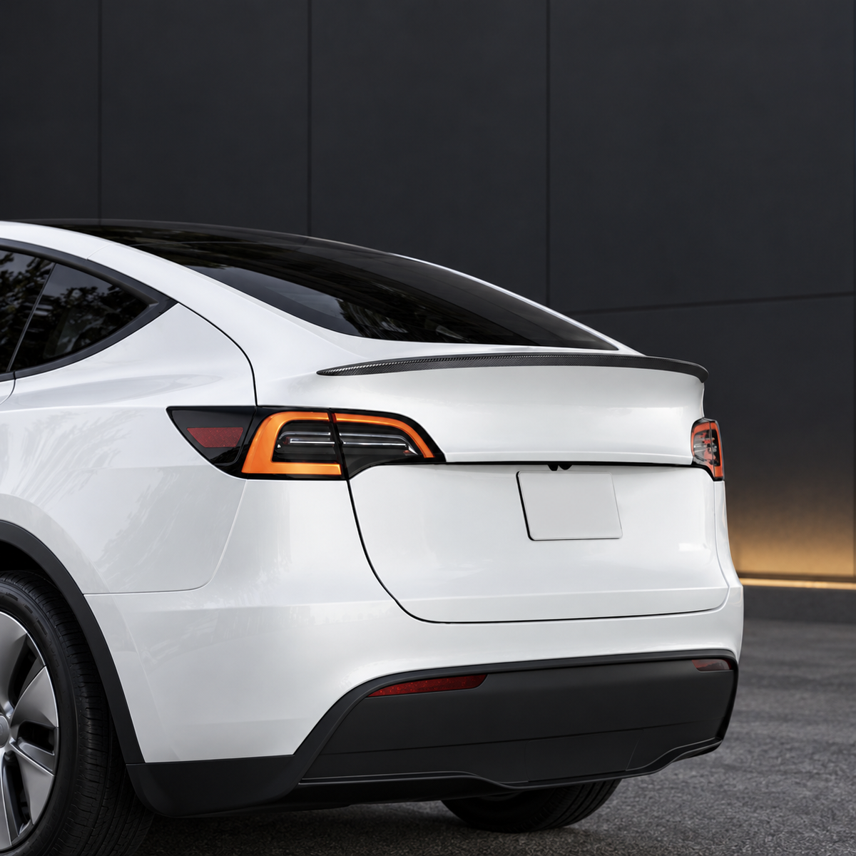 Narrow carbon-look spoiler installed along the rear hatch edge of a white legacy Model Y