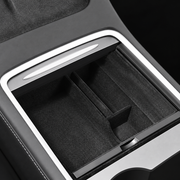 Dark flocked center console organizer with divided compartments, shown installed in a reference Tesla console.